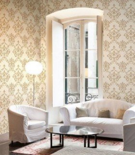 Papel pintado clásico referencia 93008 de la colección Neapolis instalado en la pared de un salón luminoso de estilo clásico, con un diseño texturizado de damascos florales en tonos dorados y fondo crema.